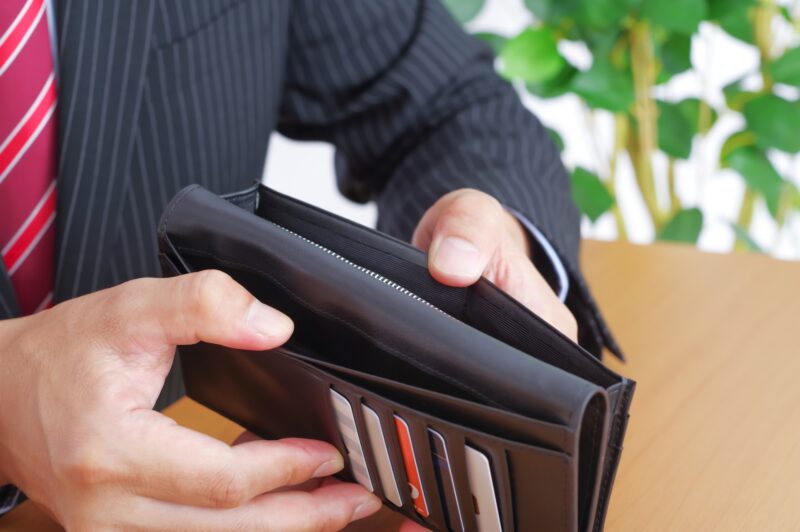 空っぽの財布を広げるワイシャツ姿の男性