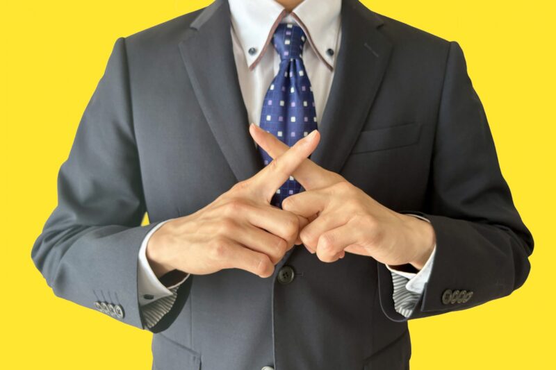 指でバツを作るスーツの男性