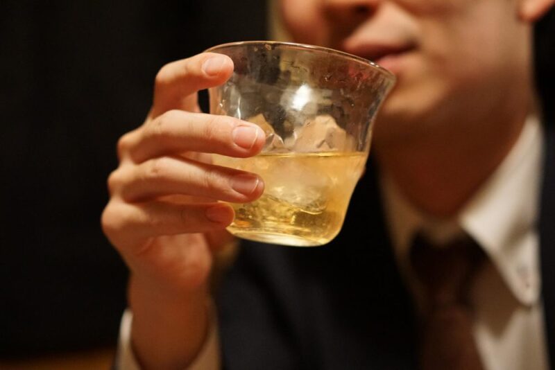 グラスのお酒を口にするスーツ姿の男性