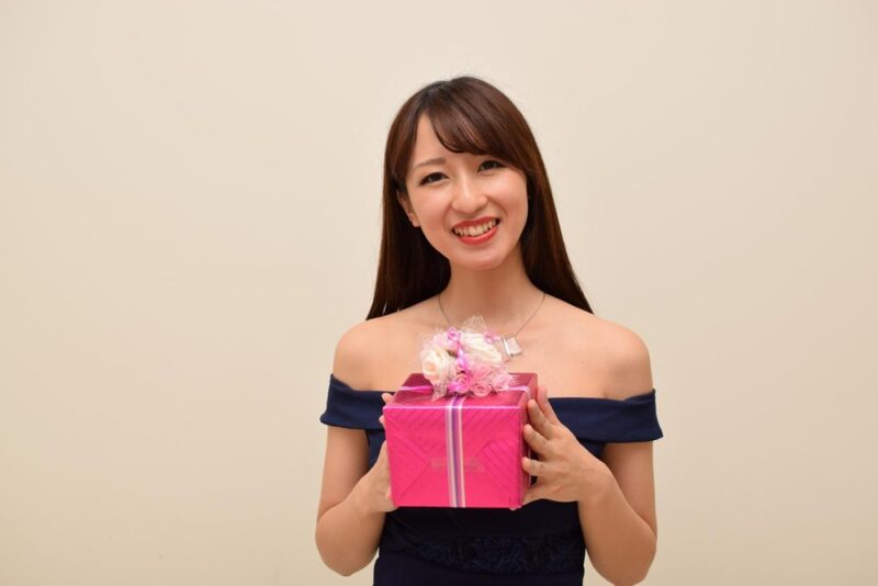 ピンクのプレゼントボックスを抱えて微笑むドレス姿の女性