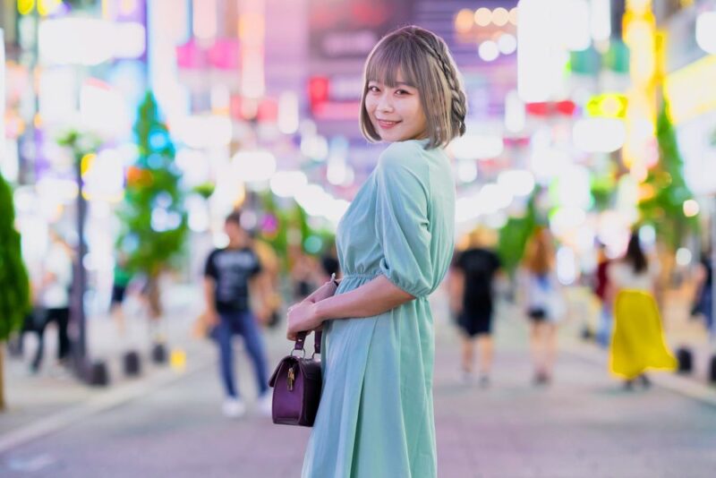 夜の繁華街を歩く緑のワンピース姿の女性